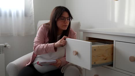 pregnant woman opening the dresser drawers of baby's room and checking them