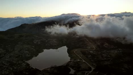 desde un punto de vista aéreo, he aquí una vista panorámica del pico más alto de portugal en la serra de estrella, donde densas formaciones de nubes comparten el cielo con un telón de fondo de una puesta de sol naciente
