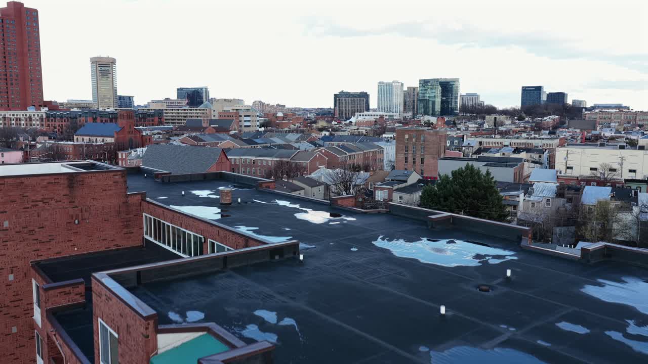 Aerial view rising past red brick apartment buildings toward the Baltimore skyline, showing urban rooftops and modern high-rise towers in distance. America town in Maryland, USA. Wide shot