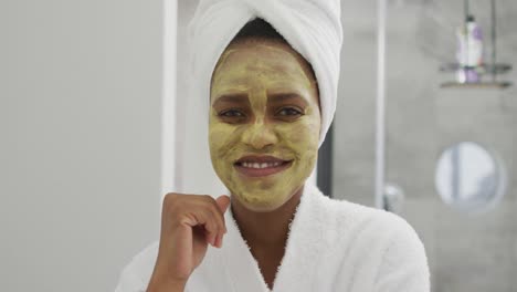 retrato de una feliz mujer afroamericana con una máscara de belleza en la cara, sonriendo en el baño