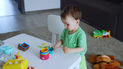 beautiful baby toy in green t-shirt stand near the desk. little kid is focused on the toys. top view.