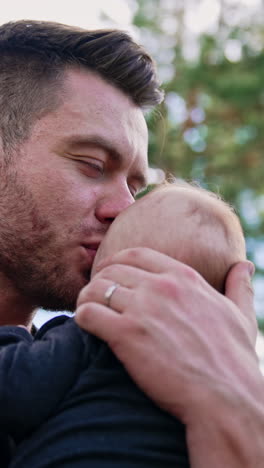muscular caucasian bearded man holding his newborn son. loving dad kisses his beloved son holding him tenderly. vertical video