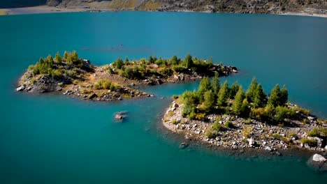 aerial flyover over forested islands with sunlit trees in the turquoise waters of lac de salanfe in valais, switzerland on a sunny autumn day in the swiss alps