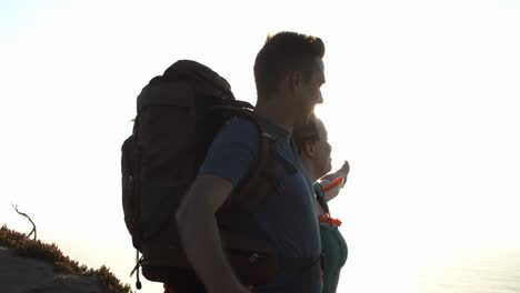 Couple-of-excited-tourists-with-backpacks-standing-at-cliff