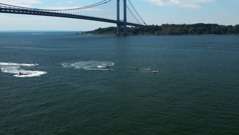 aerial-dolly-shot-forward-toward-a-few-jet-ski-riders-circling-on-the-waters-below-the-Verrazano-Narrows-Bridge-in-Brooklyn,-New-York-with-a-view-of-the-bridge---Staten-Island-in-the-background