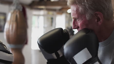 senior male boxer with younger female coach in gym using training gloves