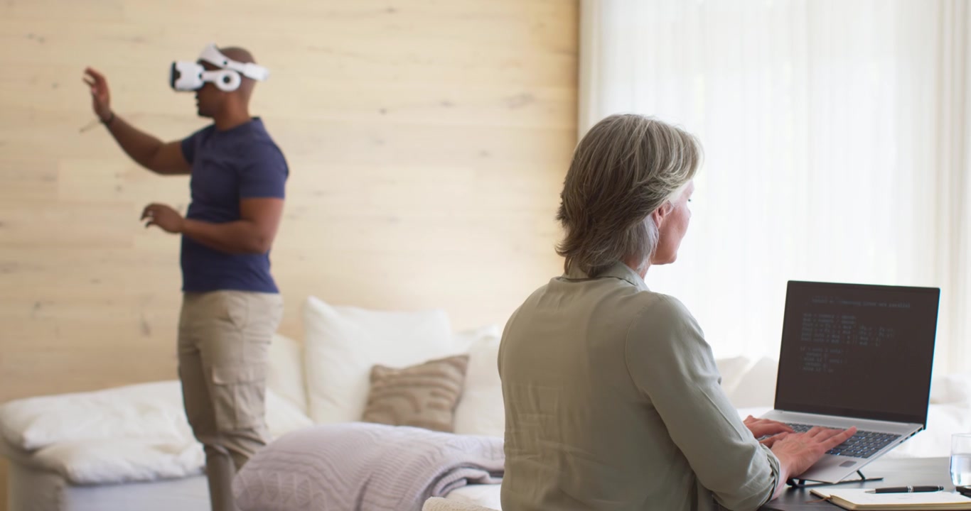 Coppia con donna anziana che digita al laptop a casa mentre l'uomo indossa un visore VR bianco.