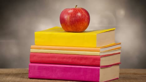 animation of stack of books with red apple on top over glowing lights