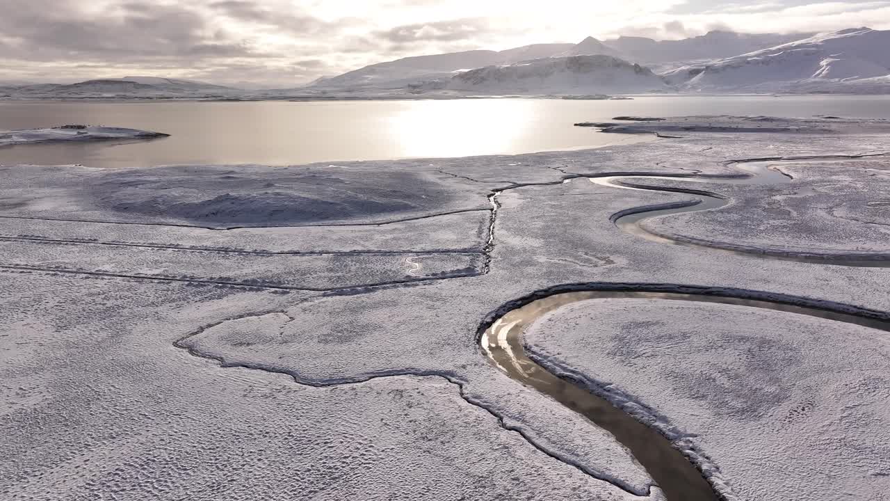 Aerial view of a frozen river winding through a snow-covered delta in Borgarfjörður, Iceland