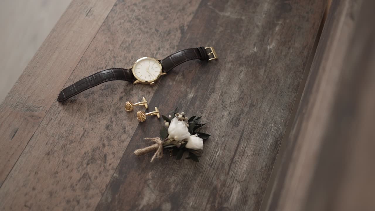 Montre en or, boutons de manchette et boutonnière disposés sur une table en bois rustique.