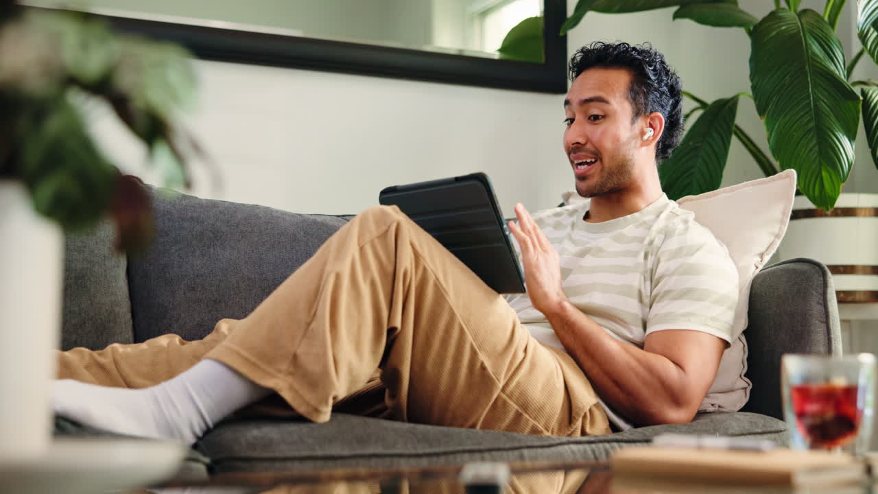Happy Young Man Relaxing on Couch and Video Calling on Tablet