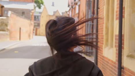 Rear-View-Of-Young-Woman-Exercising-Running-Along-Urban-Street-Wearing-Wireless-Earbuds-Before-Resting