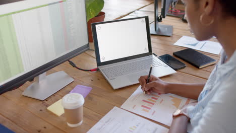 A-young-African-American-professional-examines-business-graphs-on-laptop,-copy-space