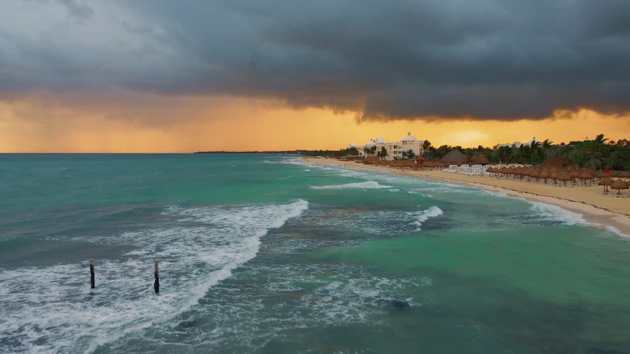 툴룸의 플라야 파라이소를 따라 부서지는 파도 위의 공중, 머리 위에 짙은 폭풍우 구름, 배경에는 주황색 일몰 하늘