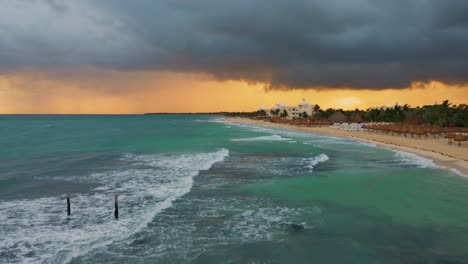 antena sobre las olas rompiendo a lo largo de playa paraíso en tulum con nubes de tormenta oscuras sobre la cabeza y el cielo naranja de la puesta de sol en el fondo