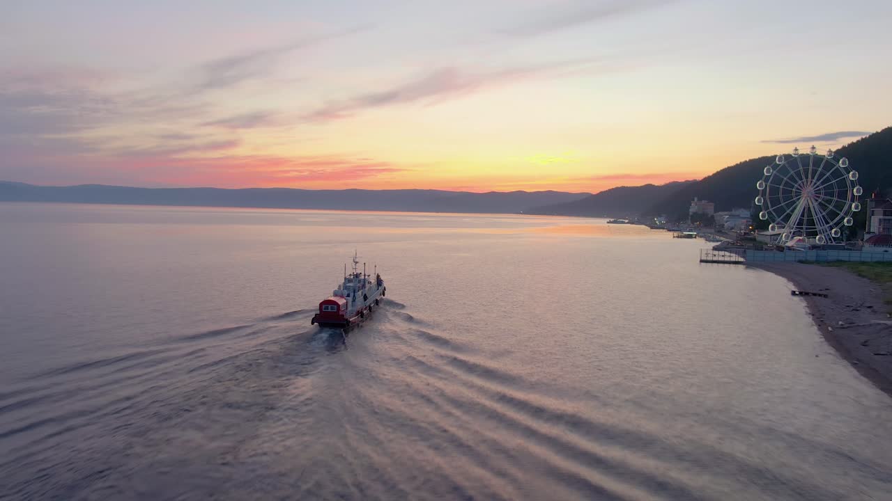 puesta de sol sobre un lago con un ferry y una rueda gigante