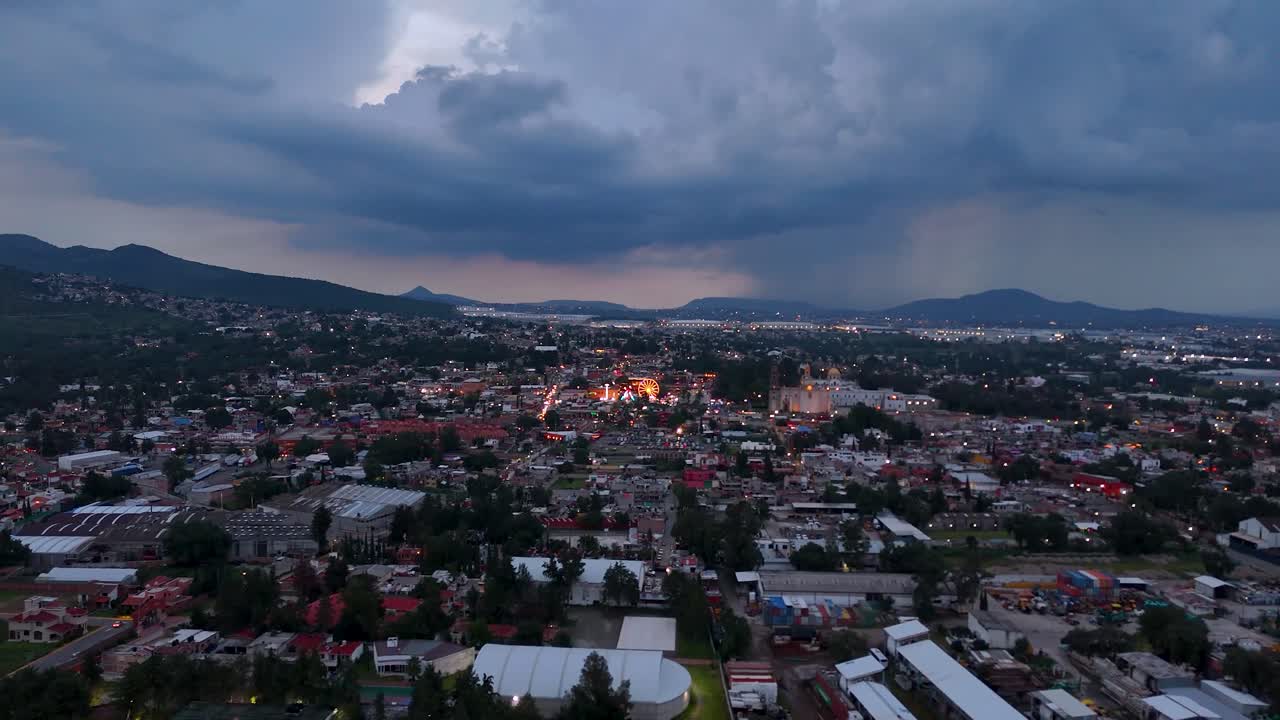 Drone shot heading toward downtown Tepotzotlán, State of Mexico, capturing the detail of rainfall and some lightning on the horizon, prior to the Independence Day celebration