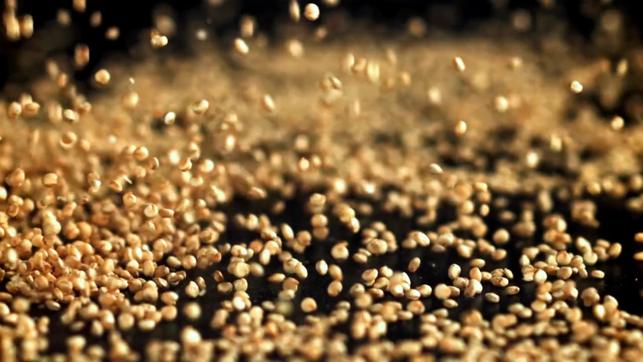 Semi di quinoa crudi che cadono al rallentatore su una superficie scura