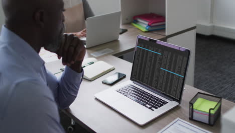 hombre afroamericano sentado en el escritorio viendo el procesamiento de datos de codificación en la pantalla del portátil