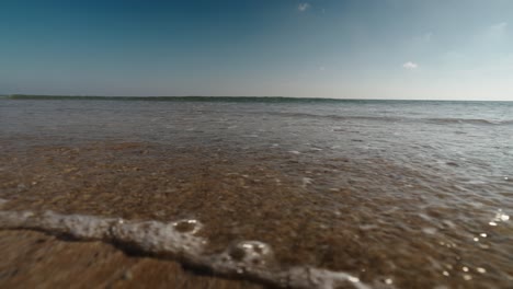 sunlight glistens on clear shallow waters as gentle waves approach the sandy shoreline on a beach in algarve, portugal
