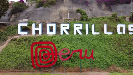 video de drones de un letrero rojo que dice "perú" y detrás de él en una colina verde, otro letrero que dice "chorrillos" el nombre del distrito en lima, perú