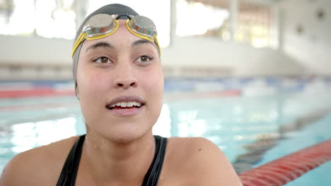 female swimmer in pool wearing goggles and swim cap, smiling after training session
