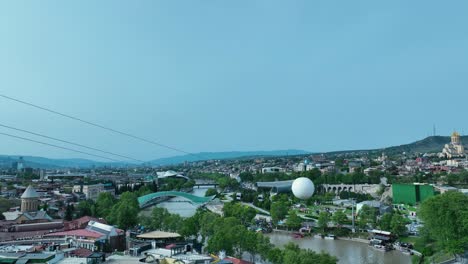 Drohnenaufnahme-Des-Alten-Tiflis-Mit-Friedensbrücke-Und-Seilbahn-Und-Samiba-Kirche-Bei-Sonnigem-Wetter