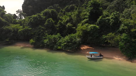 Static-drone-view-of-two-people-and-a-speed-boat-anchored-at-a-deserted-beach-at-Pang-Na-Bay-on-Koh-Yao-Noi-Island-in-Thailand