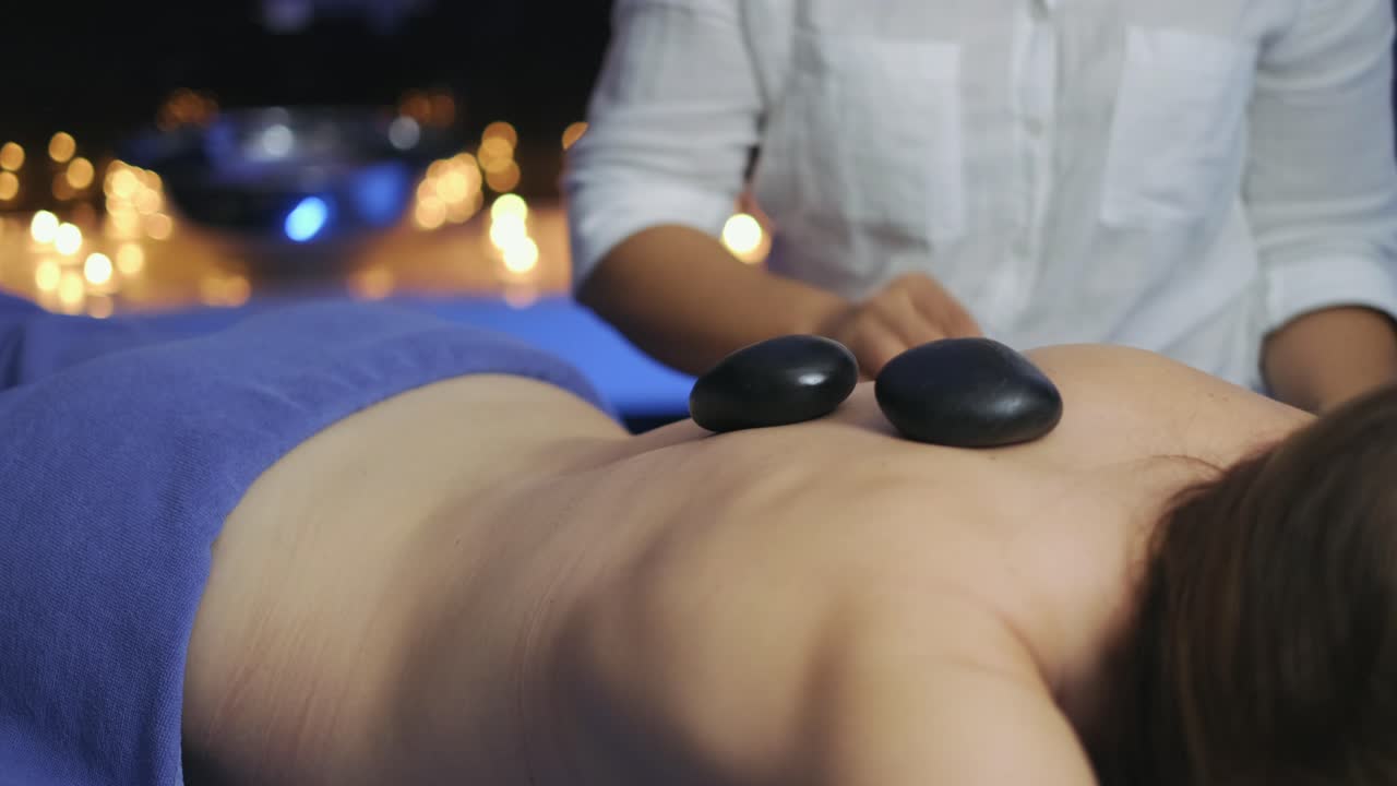 I massagerummet lægger massøsen varme sten på kvindens ryg