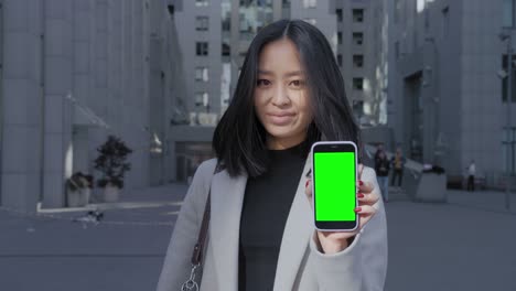young adult asian student showing a smart phone with a green screen chroma key in the city