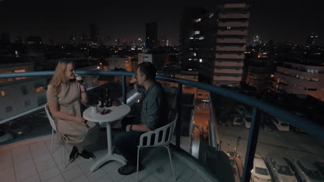 man and woman having drinks on the rooftop cafe in night city