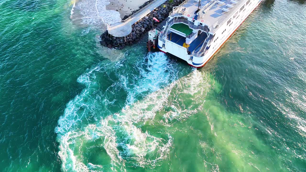 Aerial view of a ferry docking at Queenscliff terminal, showcasing vibrant turquoise waters and dynamic wave patterns