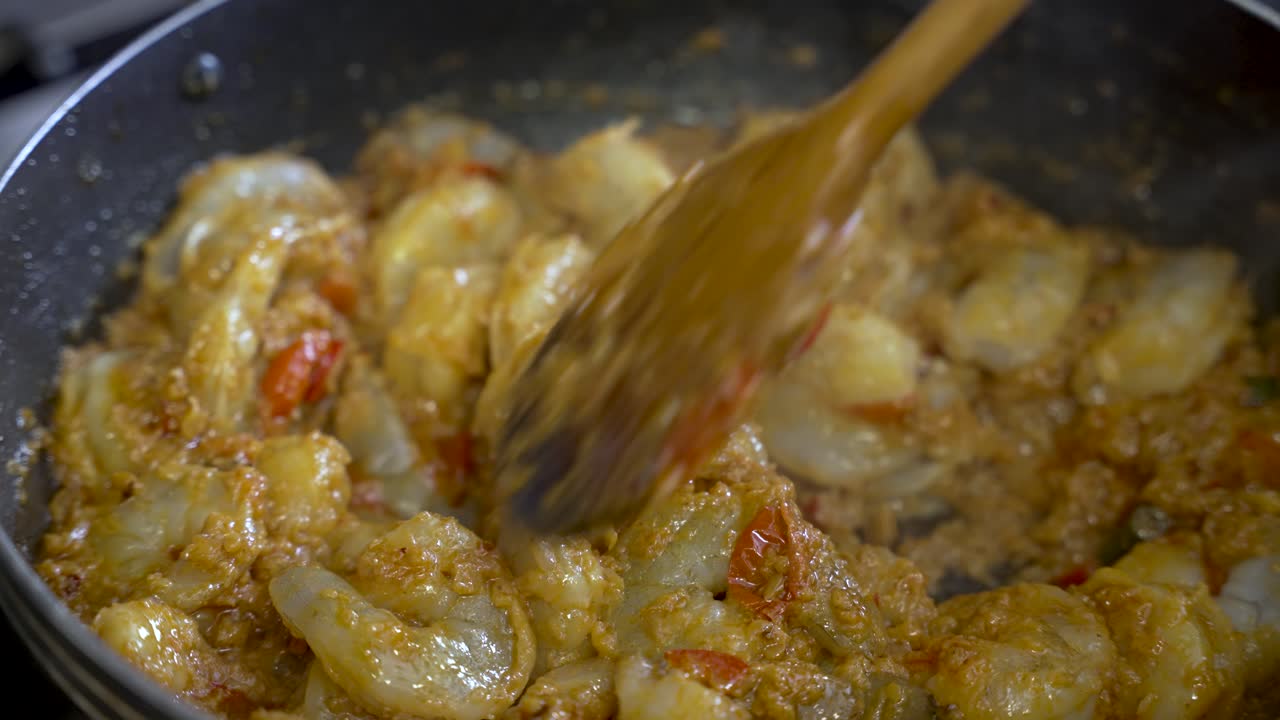한 사람이 나무 막대기를 사용하여 새우 커리를 으면서 맛있는 식사를 근접적으로 볼 수 있으며, 요리 전문성의 개념을 구현합니다.