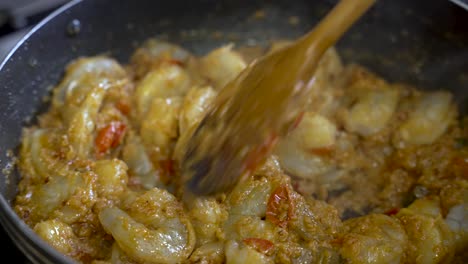 una persona usa un palo de madera para agitar el curry de camarón, ofreciendo una vista de cerca de la deliciosa comida en un plato, encarnando el concepto de experiencia culinaria