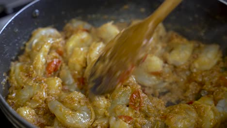 a person uses a wooden stick to stir prawn curry, offering a close-up view of the delicious meal in a dish, embodying the concept of culinary expertise