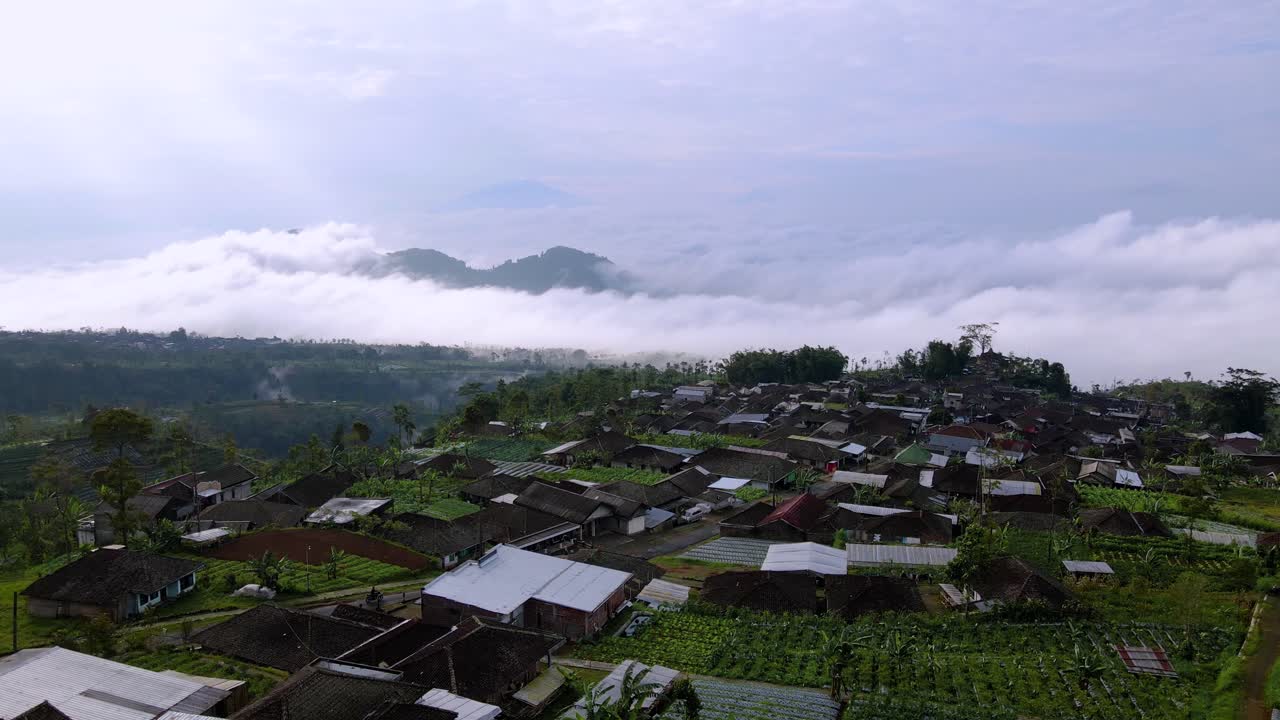sobrevuelo aéreo de la aldea rural, con vistas al monte sumbing, nubes etéreas