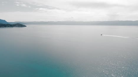 Aerial-shot-of-a-boat-moving-toward-a-bay-on-turquoise-water-around-Macedonian-Ohrid-Lake-in-Southern-Europe