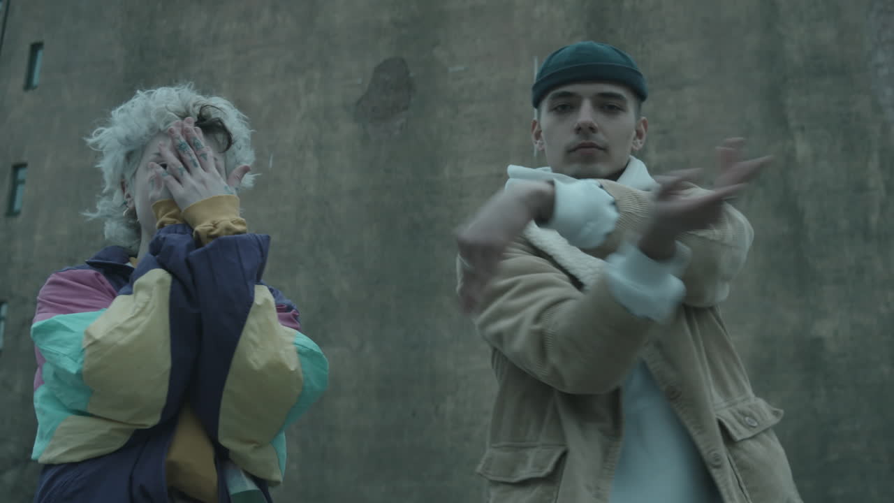 트렌디한 옷을 입은 커플이 야외에서 카메라 앞에서 춤을 추고 있습니다.