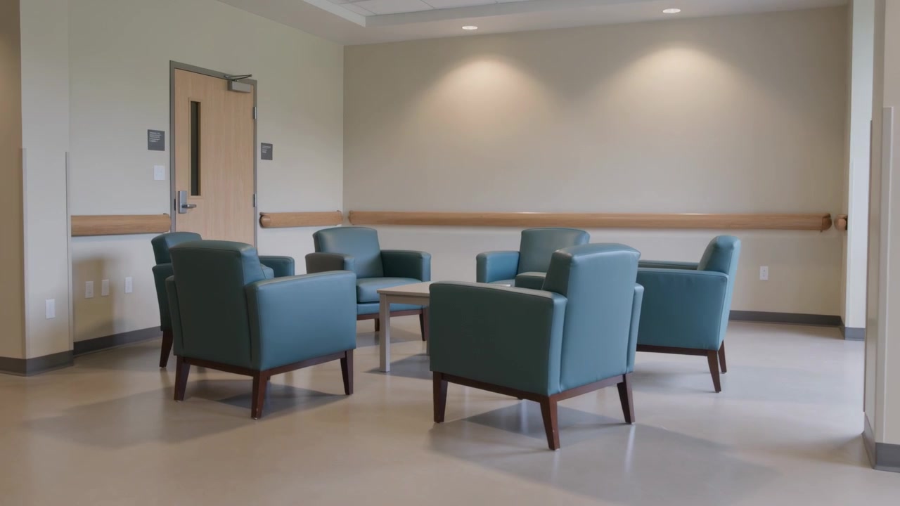 Panning camera centering six teal armchairs in care facility lounge, revealing wooden table
