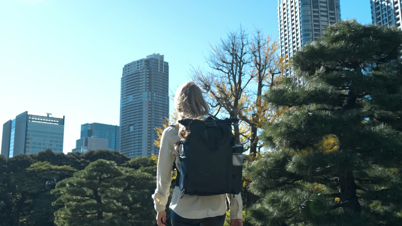 A girl walks through the beautiful pathways of Hamarikyu Gardens, Tokyo, with the modern city buildings in the background.