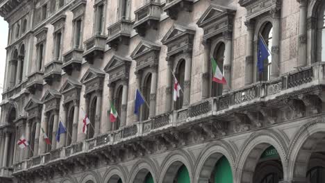 many italian ,european and milan flags in the wind on the ancient palace in the center of milan