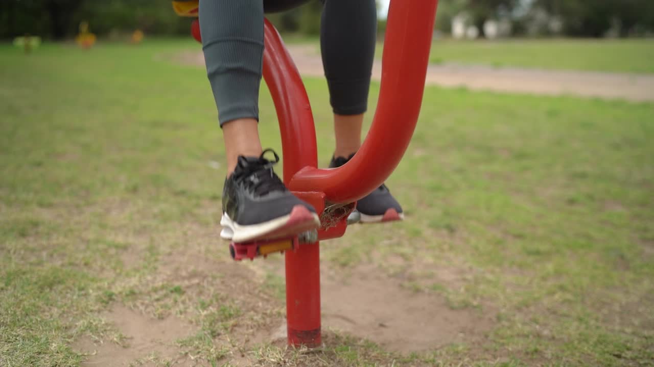 los pies de la dama mientras usa un dispositivo de ejercicio de pedal en el parque - de cerca