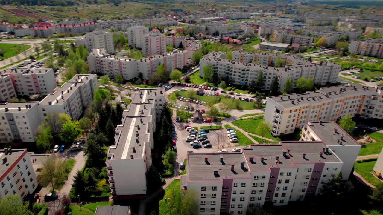 Aerial view of a Polish town with apartment blocks and green hills. A blend of urban living and natural landscape under bright skies in a peaceful residential setting