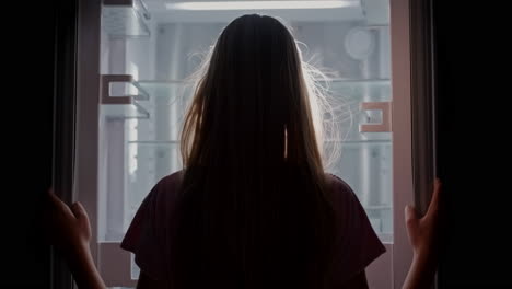 a young woman opens the doors of an empty refrigerator.