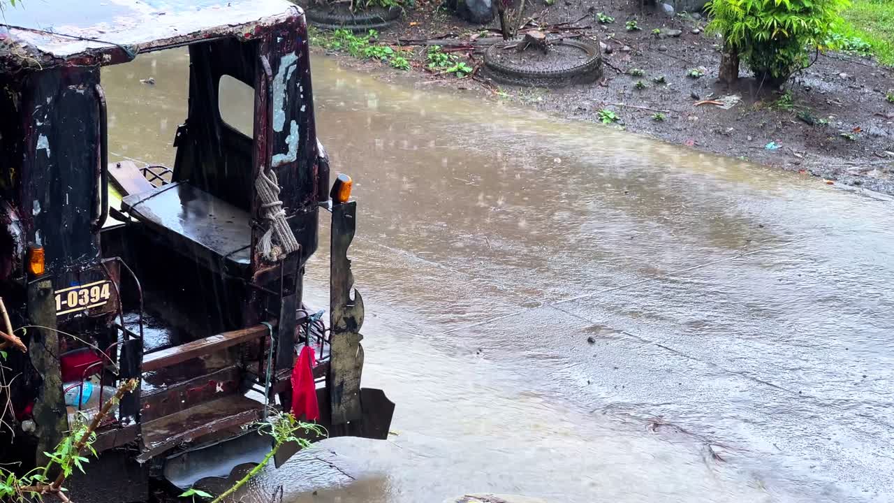 Rusty rickshaw sits abandoned as rain pours in a rural setting. Ideal for themes of hardship, decay, weather, or cinematic storytelling