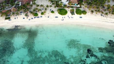 Aerial-bird's-eye-drone-view-of-a-beautiful-tropical-vacation-beach-with-crystal-clear-blue-water,-white-sand,-palm-trees,-lounge-chairs-at-a-resort-in-Riviera-Maya,-Mexico-near-Cancun