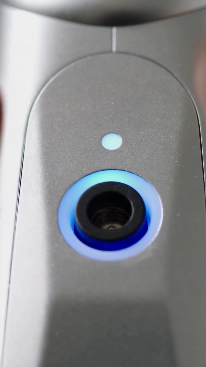 Vertical video: Focusing camera on gray panel close-up in room, showing blue ring and status dot