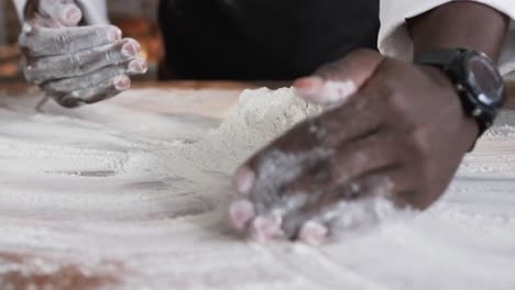 African-american-male-baker-working-in-bakery-kitchen,-gathering-flour-on-counter-in-slow-motion