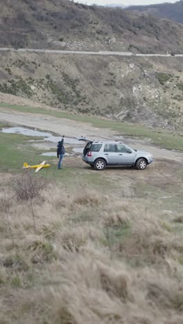 man launching model airplane near car in mountainous landscape