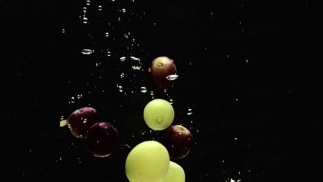 red and green grapes dropped into water with floating air bubbles, black background